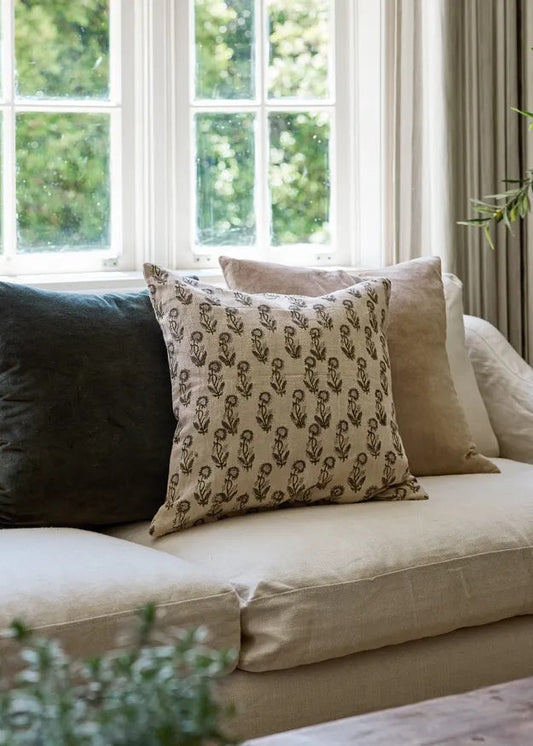 Beige sofa with decorative pillows in a room with large windows and greenery outside.
