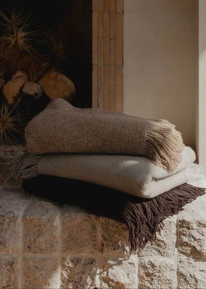 Stack of folded blankets with fringe on a stone surface