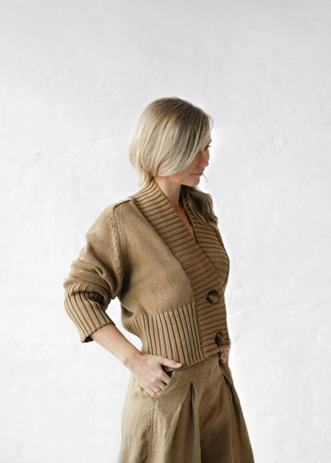Woman wearing a brown knitted cardigan and beige skirt on a white background