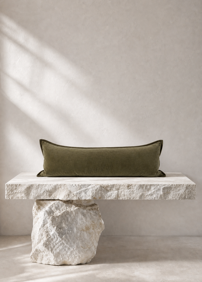An olive green rectangular throw pillow displayed on a modern floating stone bench with a rough white rock base, set against a textured beige wall with soft window shadow light.