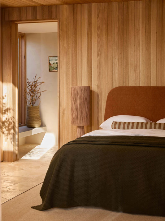 Bedroom with wooden walls and a bed with a brown headboard.