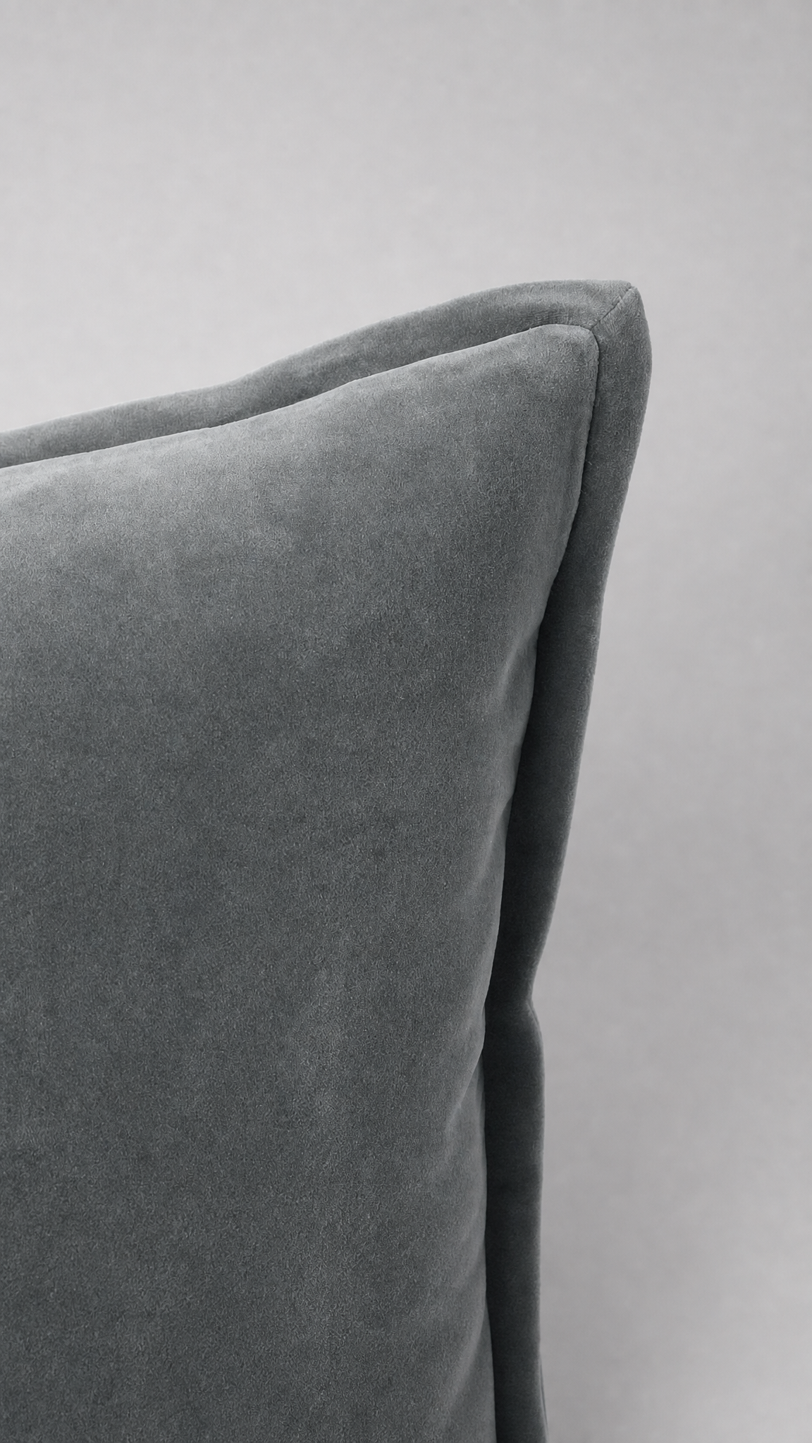 A close-up of a gray velvet throw pillow corner showing the soft fabric texture and stitched edge against a neutral gray background.