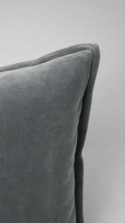 A close-up of a gray velvet throw pillow corner showing the soft fabric texture and stitched edge against a neutral gray background.