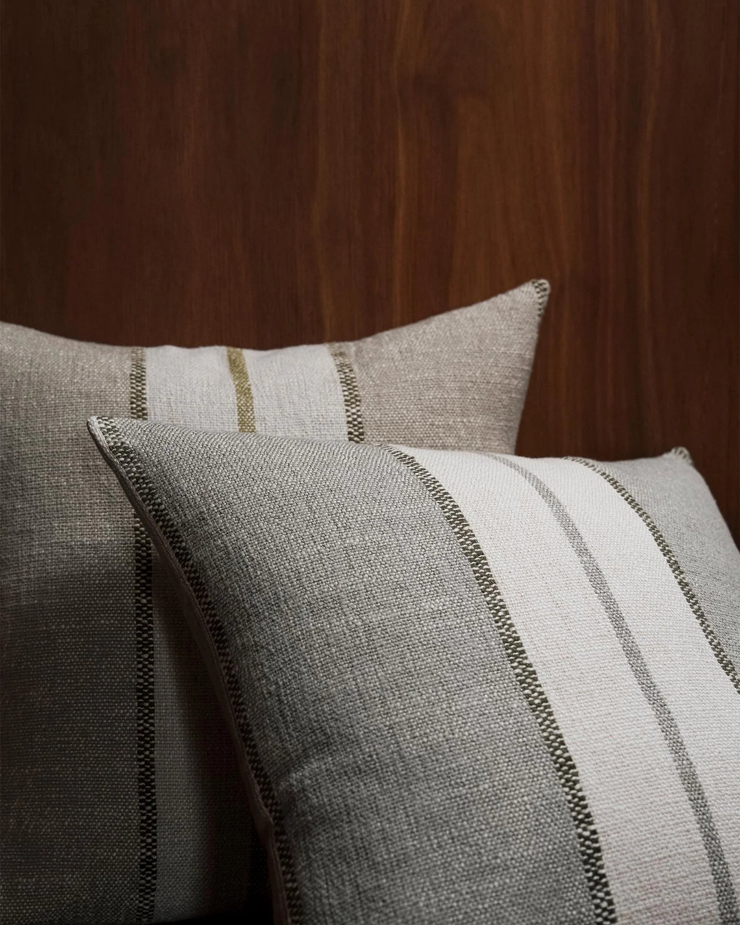 Two textured throw pillows in a neutral linen-like fabric with vertical stripes, styled against a dark wood background.