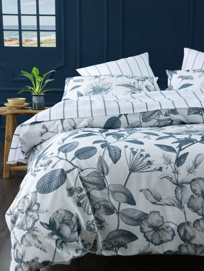 Floral and leaf patterned bedding set on a bed with a dark blue wall and window in the background.