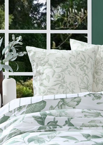 Floral-patterned bedding set with matching pillows on a bed, against a green wall and window.