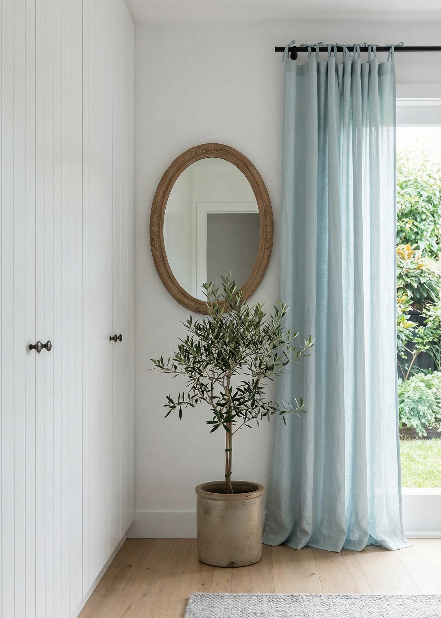 Room interior with a potted plant, round mirror, and light blue curtains.