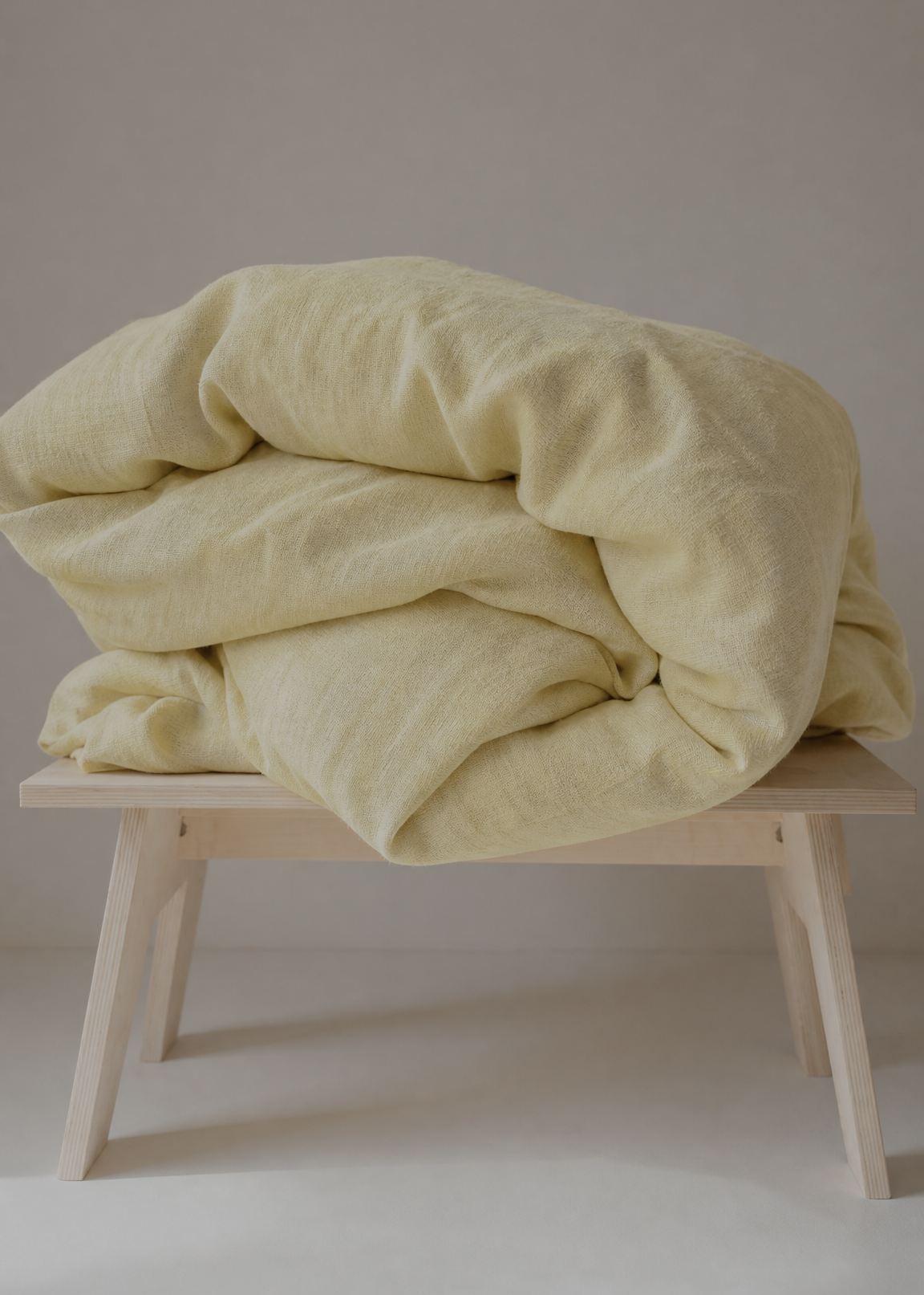 Light yellow blanket on a wooden stool against a neutral background