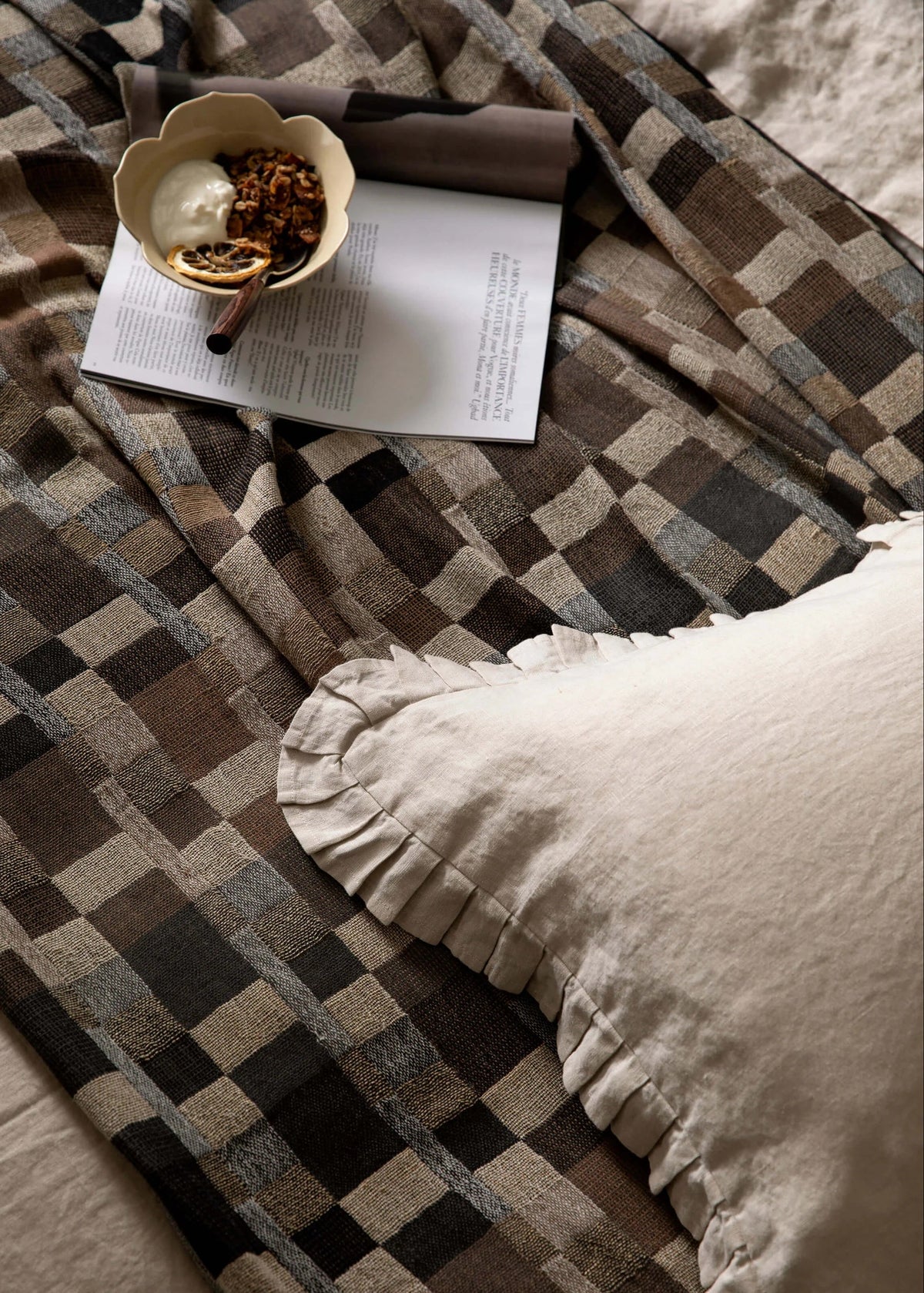 Plaid blanket with a book, teacup, and pillow on a bed