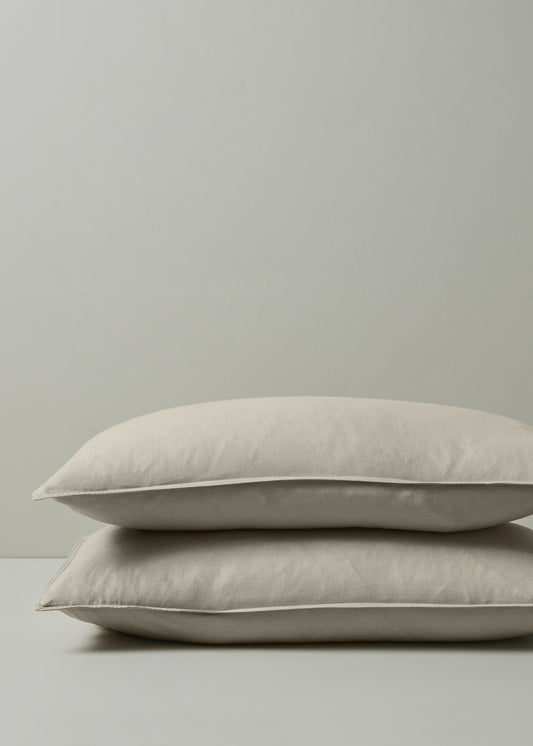 Two beige pillows stacked on a light gray surface with a neutral background