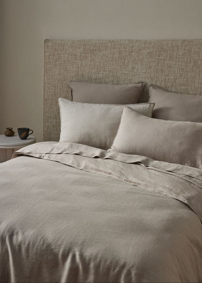 Neatly made bed with beige bedding and pillows against a neutral wall.