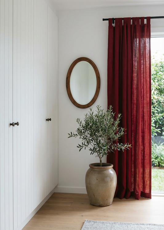 Room interior with a plant in a pot, red curtain, and round mirror.