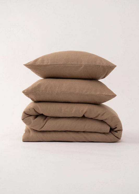Stack of brown bedding including a duvet and two pillows on a light beige background