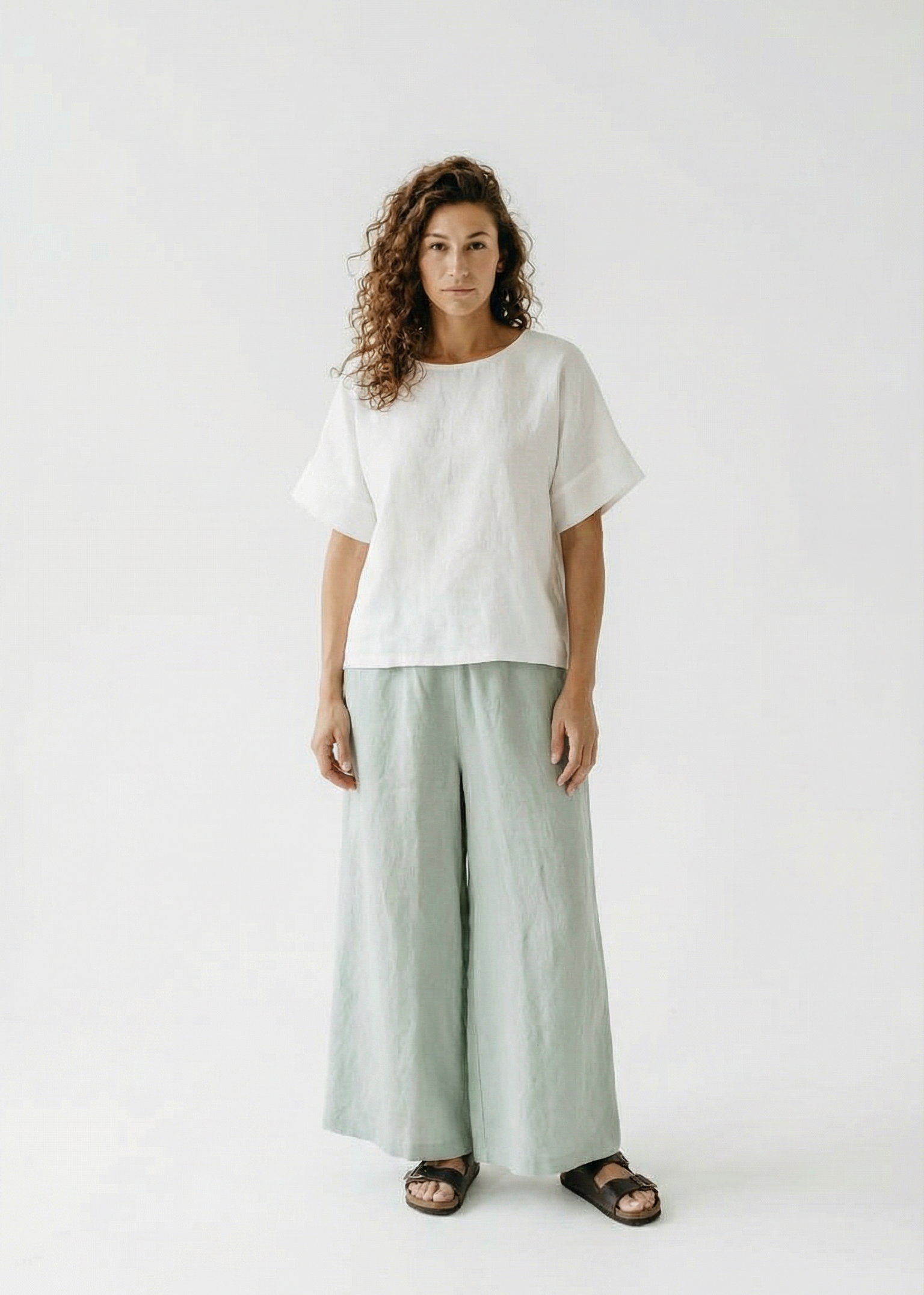 Woman wearing a white top and light green pants on a white background