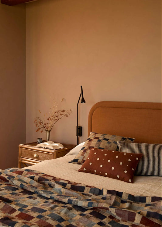 Bedroom with a bed featuring patterned bedding and pillows, a nightstand with a lamp, and a wall-mounted lamp.