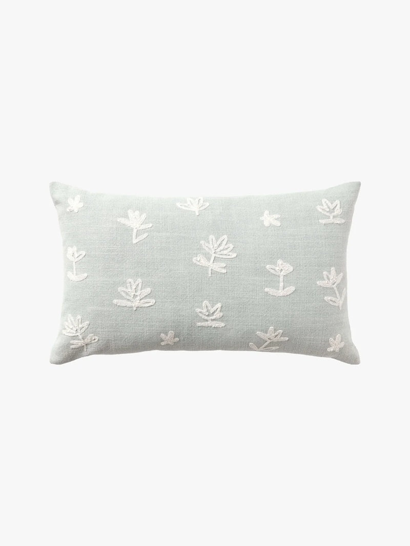 A rectangular light sage green throw pillow with white embroidered floral motifs, shown against a plain white background.