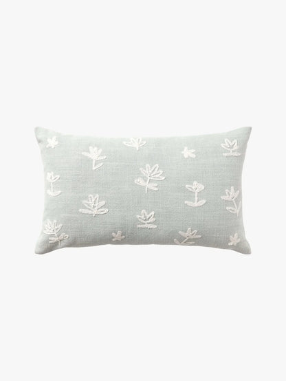 A rectangular light sage green throw pillow with white embroidered floral motifs, shown against a plain white background.