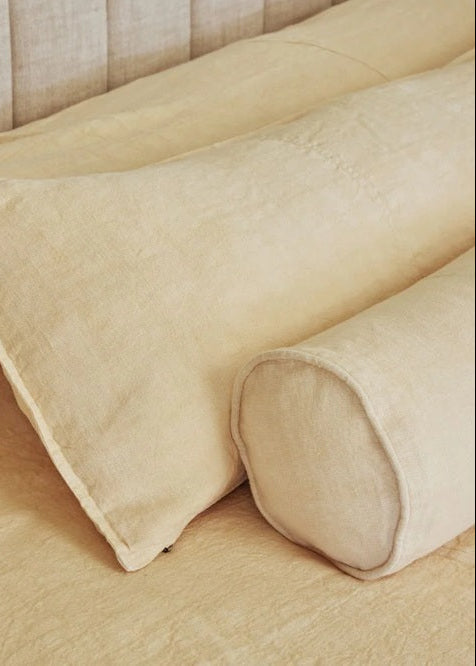 Beige linen bedding set featuring a pillowcase, matching duvet cover, and a cylindrical bolster pillow on a bed with a tufted headboard.