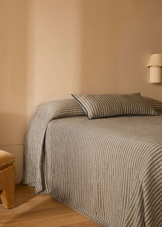 Bed with striped bedding in a room with beige walls and wooden floor.