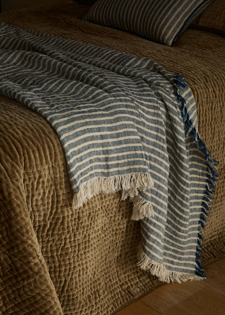 Blue and white striped blanket with fringes on a textured surface