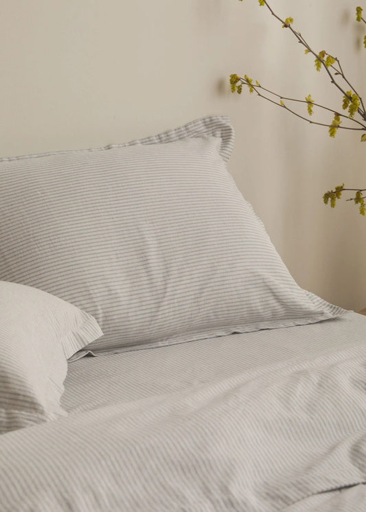 Gray striped bedding with white pillows on a bed against a beige wall.