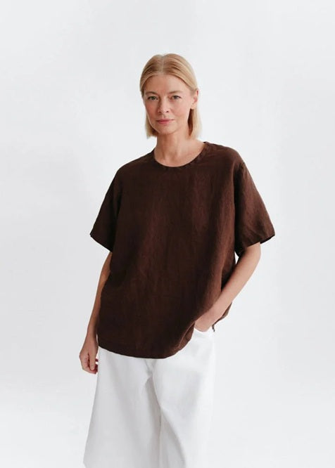 Person wearing a brown oversized t-shirt and white pants on a light gray background