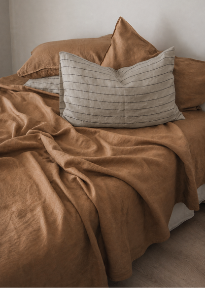 A bed styled with warm brown bedding and matching pillows, including a striped beige accent pillow, set against a neutral off-white wall.