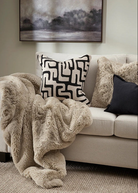 Beige sofa with a fluffy blanket and patterned pillows in a living room setting.