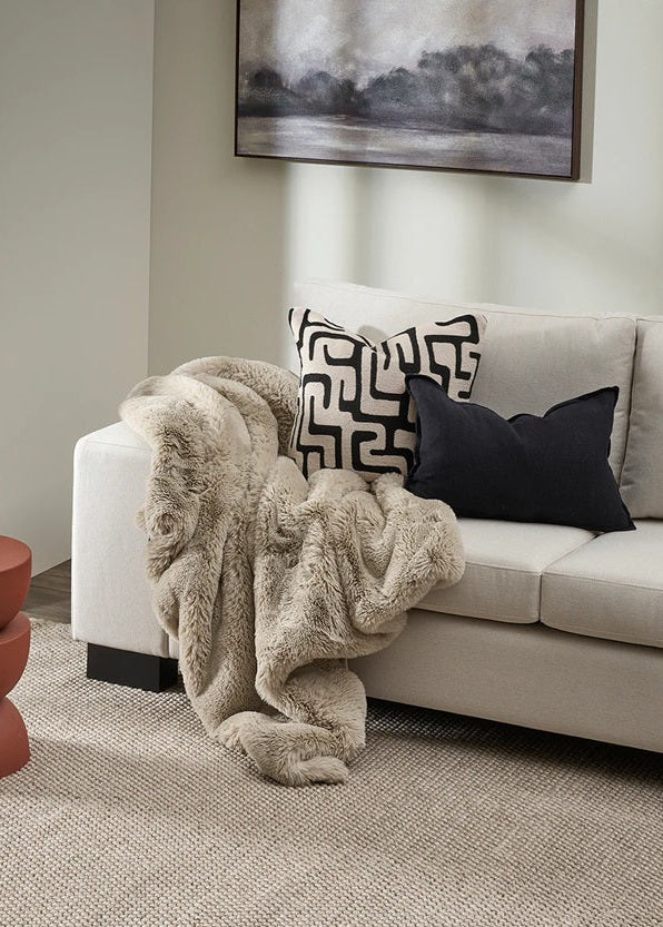 Beige sofa with decorative pillows and a fur throw blanket in a living room setting.