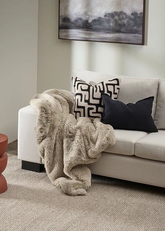 Beige sofa with decorative pillows and a fur throw blanket in a living room setting.