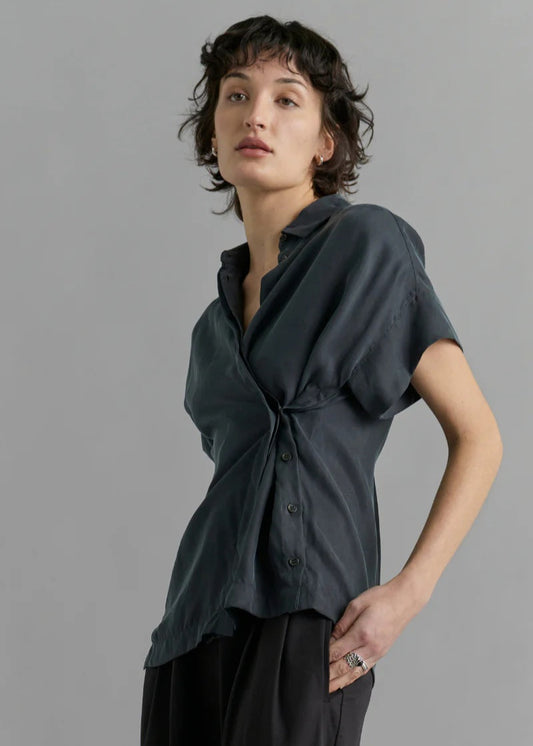 Person wearing a dark gray shirt with a knot detail on a gray background