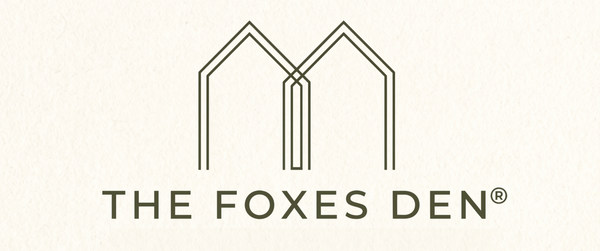 The Foxes Den logo featuring a stylized geometric 'M' above the brand name, shown in dark brown on a textured off-white background.