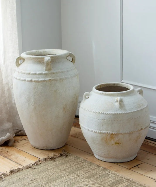 Two large white ceramic pots on a wooden floor with a neutral background