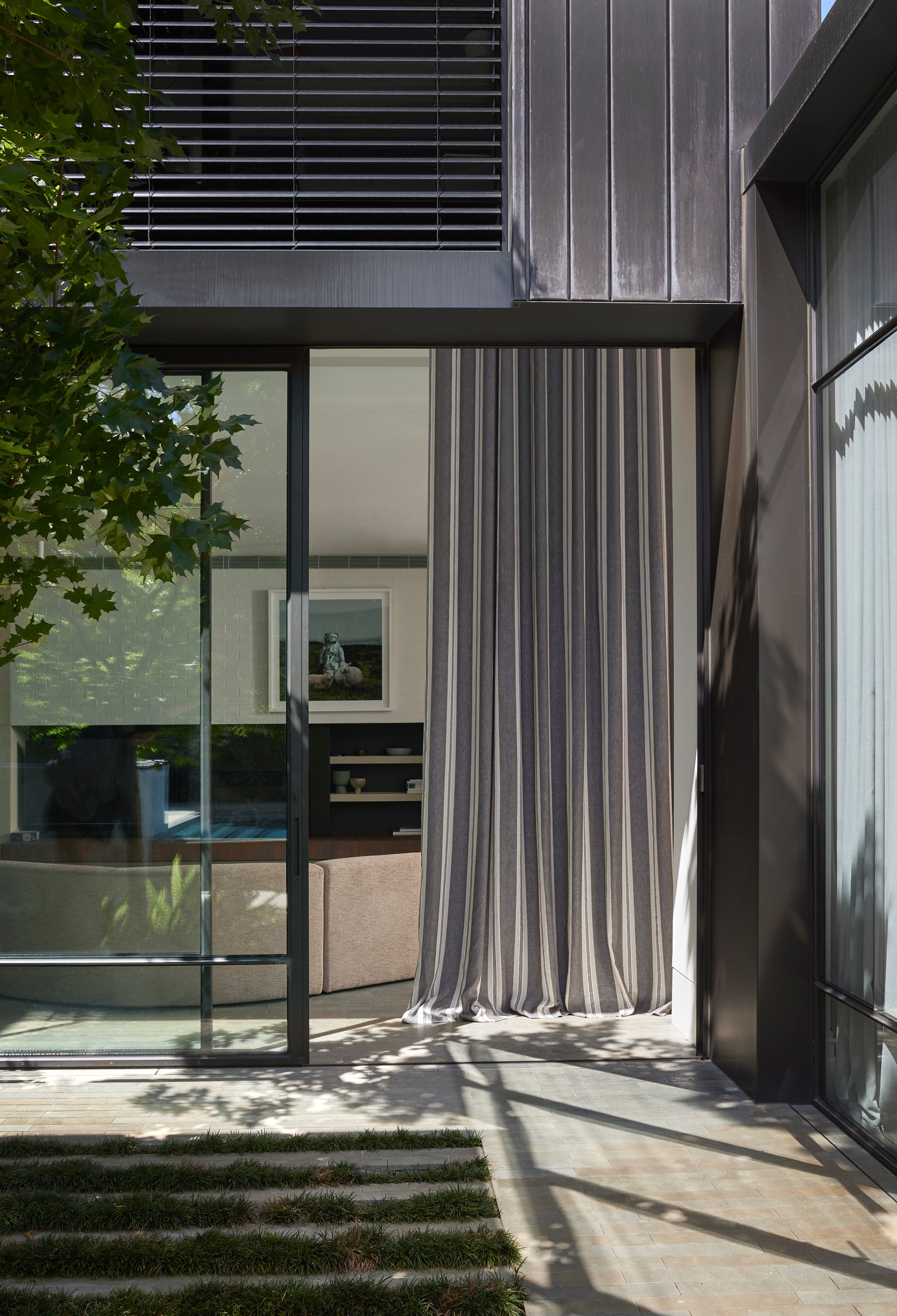 Modern architectural design with glass panels and a curtain, surrounded by greenery.