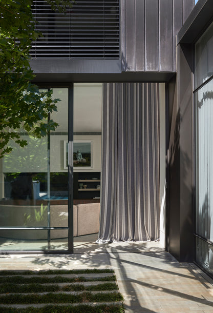 Modern architectural design with glass panels and a curtain, surrounded by greenery.