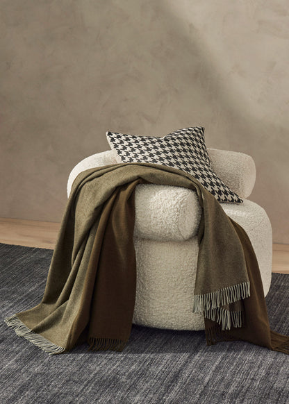 White armchair with a brown blanket and checkered pillow against a beige wall.