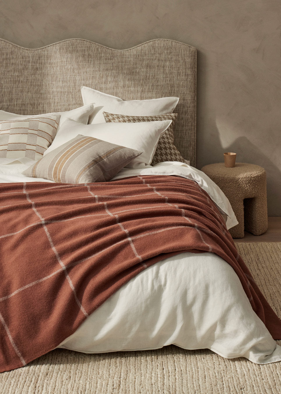 Neatly made bed with brown checkered blanket and white pillows against a neutral wall.
