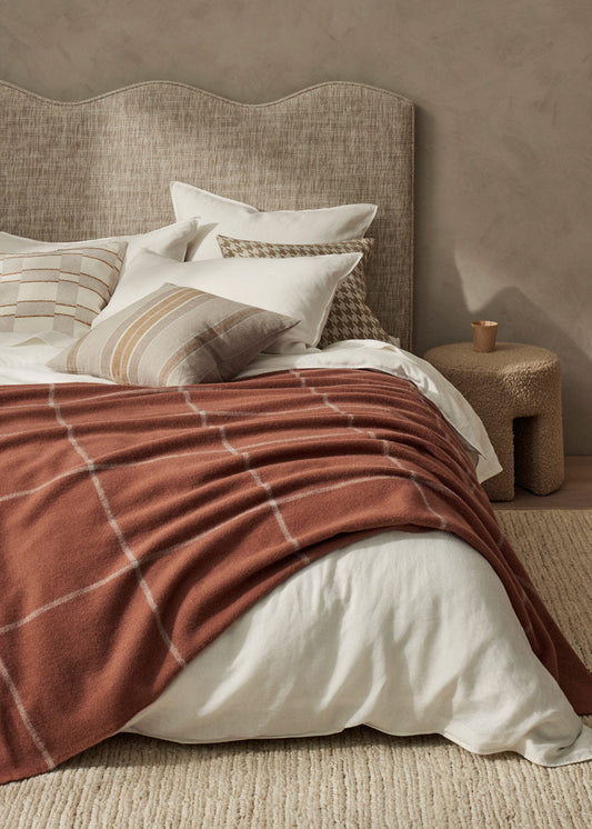 Neatly made bed with brown checkered blanket and white pillows against a neutral wall.