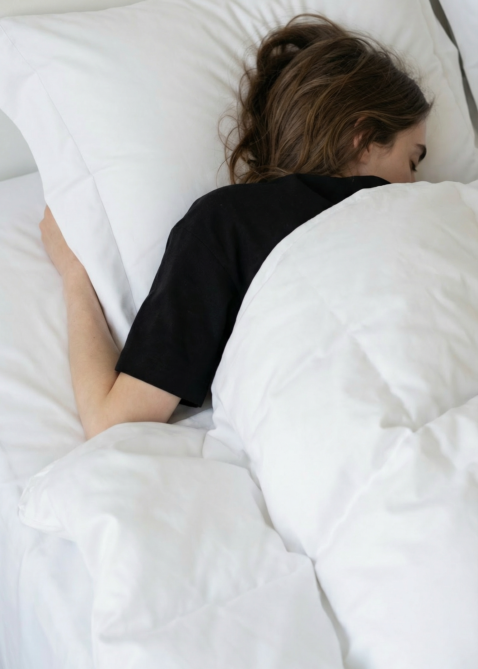 Person lying in bed under white sheets and pillows