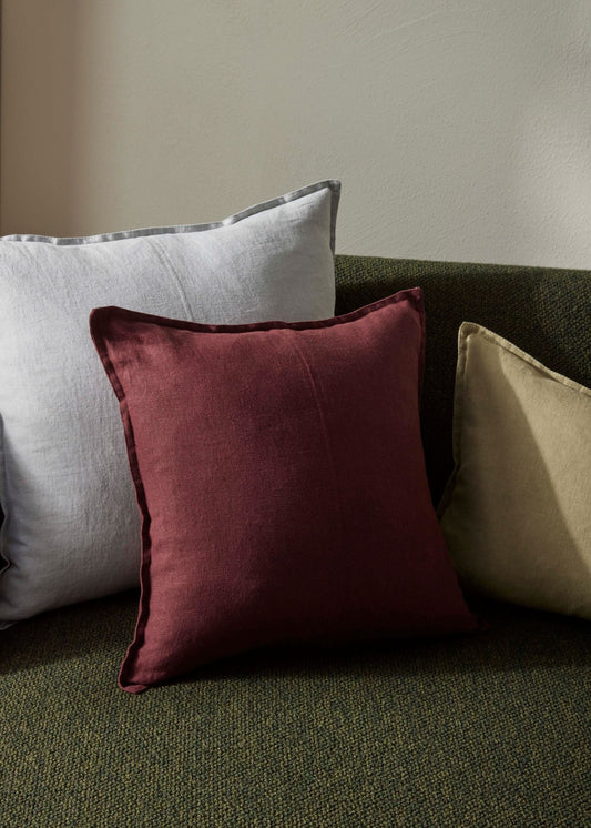 Three pillows in gray, red, and beige on a green sofa against a neutral wall.