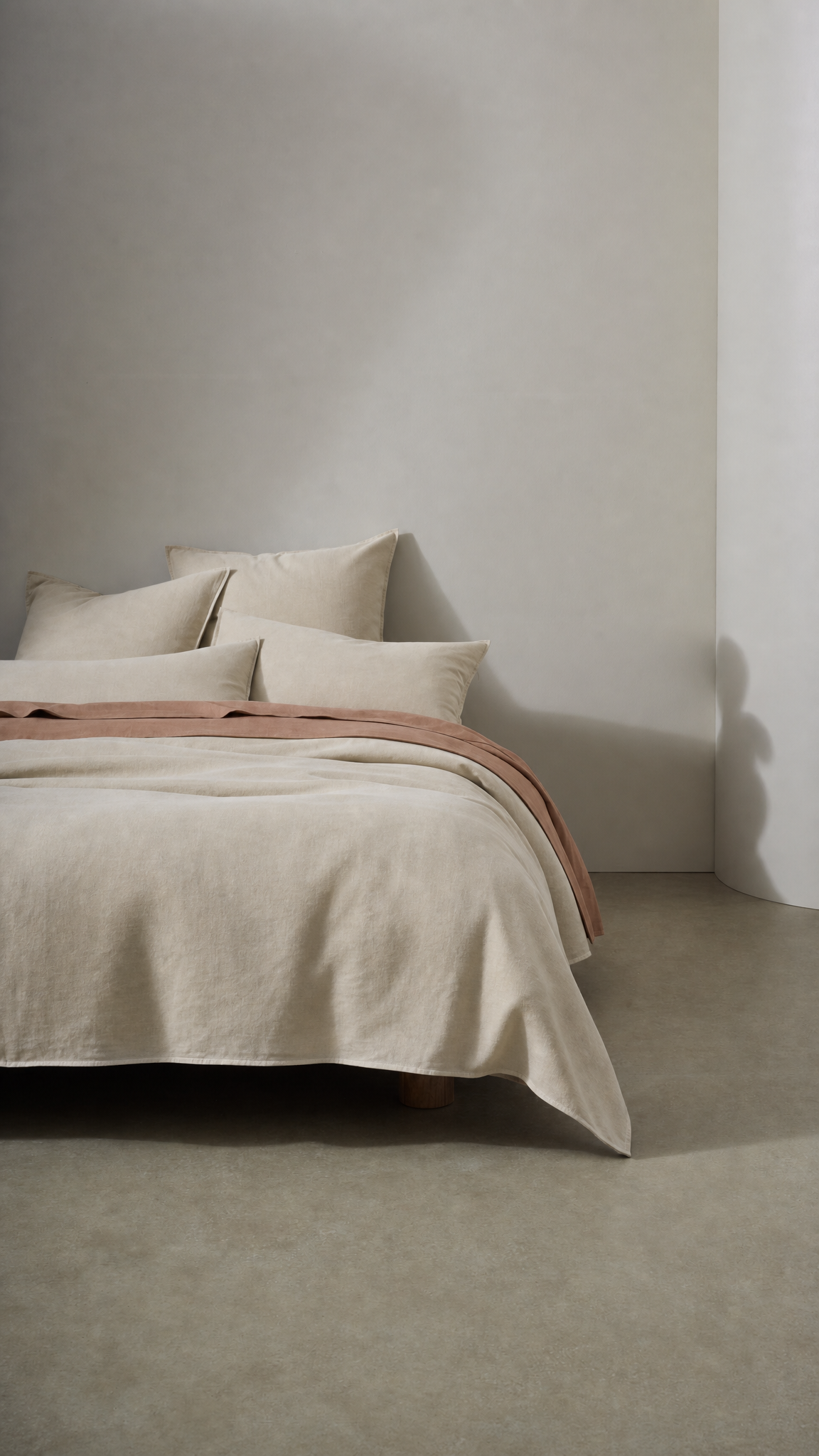 Neatly made bed with beige bedding against a plain wall.