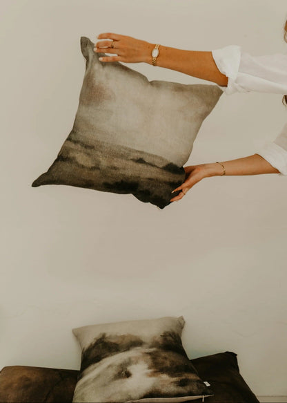 Person holding a decorative pillow with a neutral color palette against a plain background