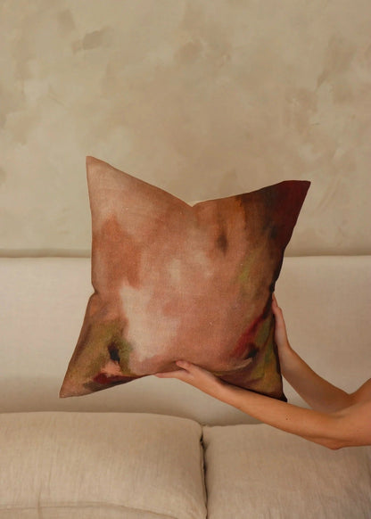Person holding a decorative pillow against a beige wall.