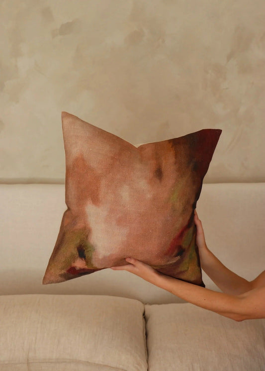 Person holding a decorative pillow against a beige wall.