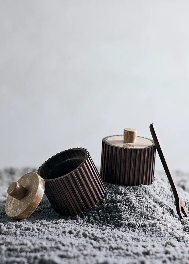 Three brown ceramic containers with wooden lids on a textured surface