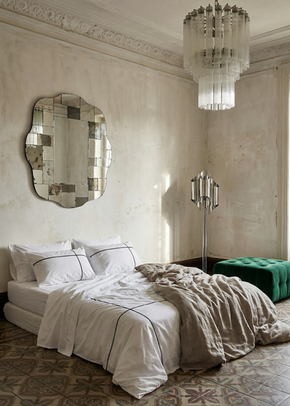 Luxurious bedroom with a large mirror, chandelier, and green ottoman.