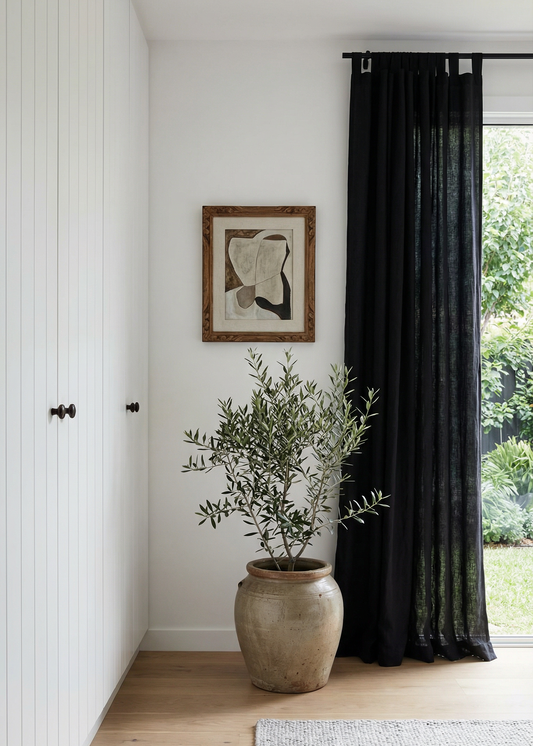 Room interior with a plant in a pot, framed picture on the wall, and black curtains.