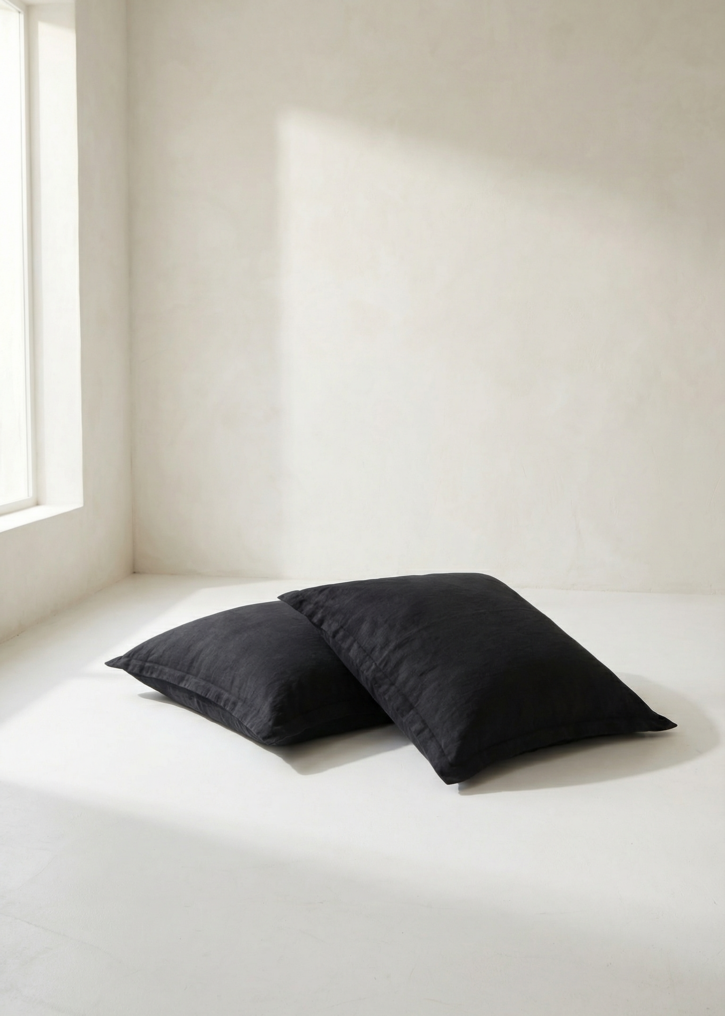 Two black pillows on a white bed in a minimalistic room with a window.