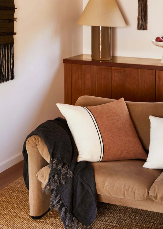 Brown sofa with decorative pillows and a lamp on a wooden sideboard in a room.