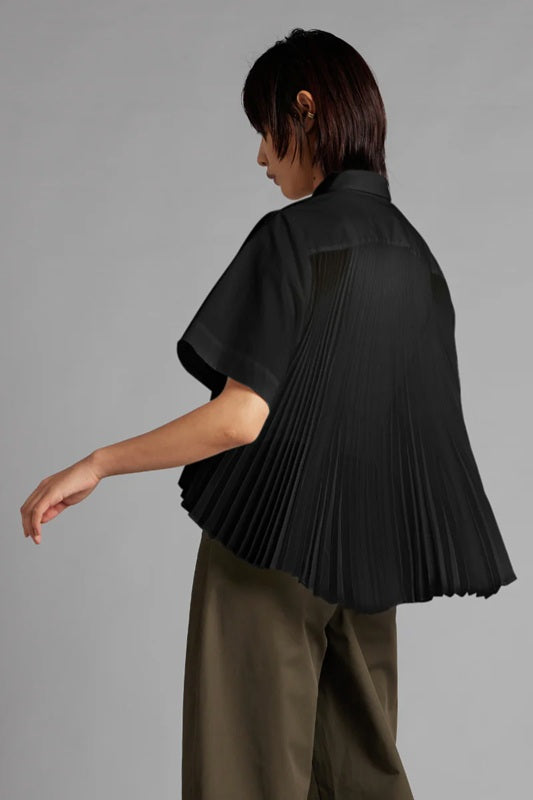 Person wearing a black pleated top and green pants on a gray background